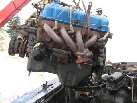 1992 Ford F-250 - Engine with blue valve covers and rusted exhaust manifolds is being lifted by a red crane.