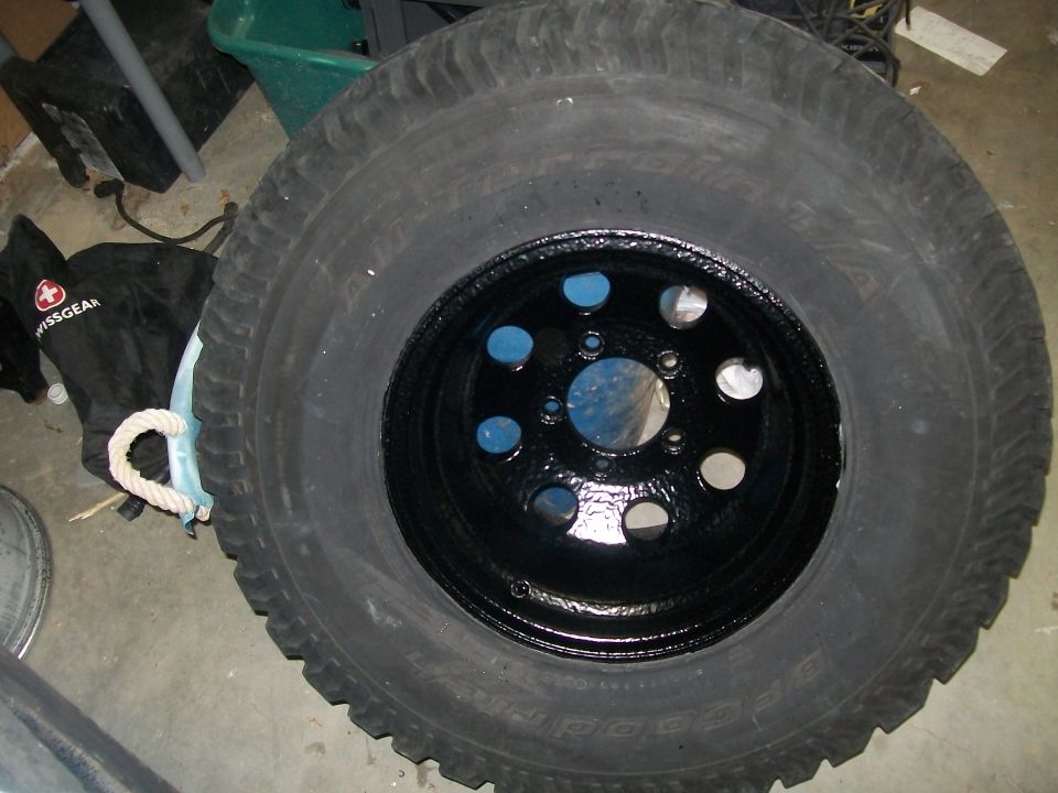 Mud terrain tire mounted on a black steel wheel lying on a garage floor