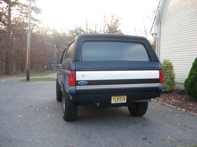 Rear view of dark blue Ford Bronco with off-road tires and NJ plate, parked in a driveway