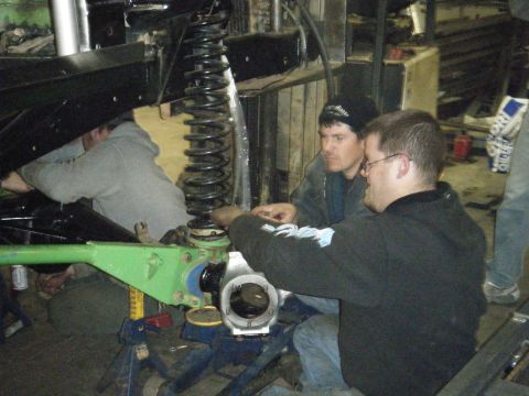 1978 Ford Bronco - Three men are working on the suspension of a vehicle in a garage.
