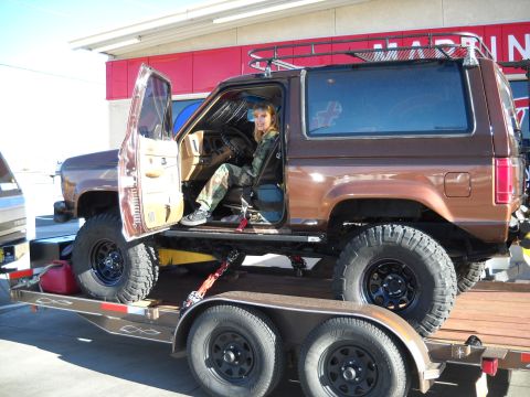1986 Ford Bronco II - A woman sits in the driver's seat of a brown Ford Bronco II loaded onto a trailer.
