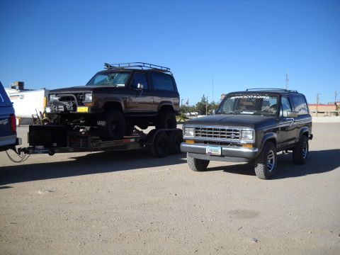 1986 Ford Bronco II - Two 1986 Ford Bronco II SUVs are parked outdoors, with one loaded onto a trailer.