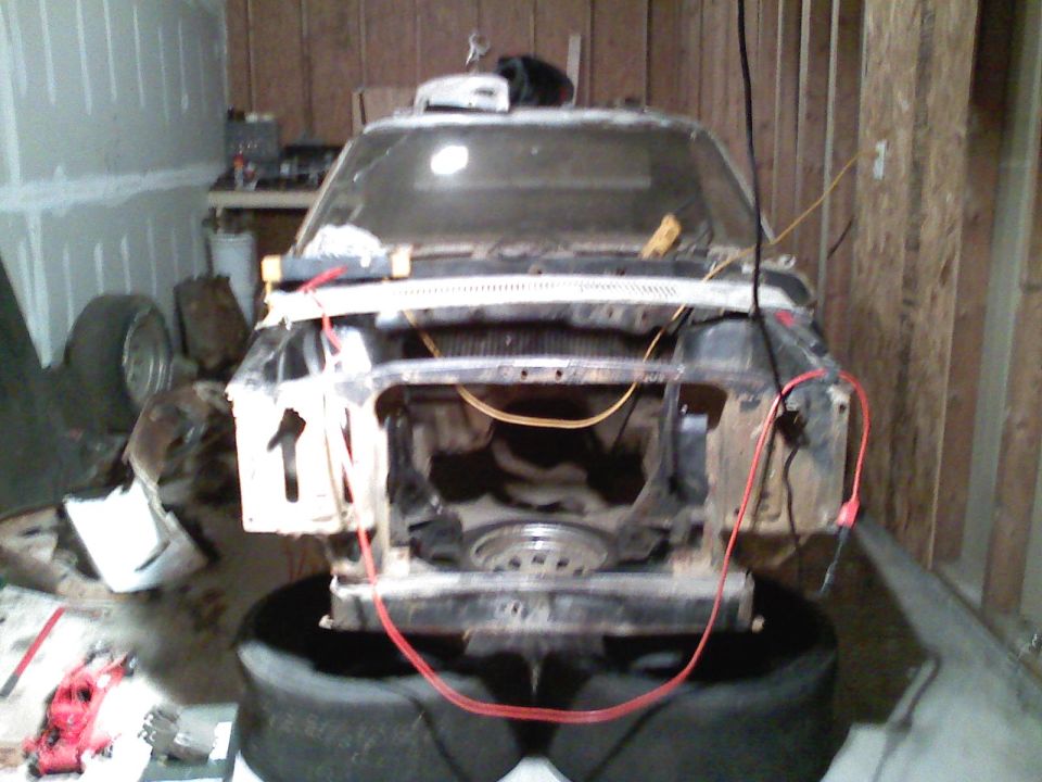 Car front end, missing grille and headlights, sitting on tires in a garage