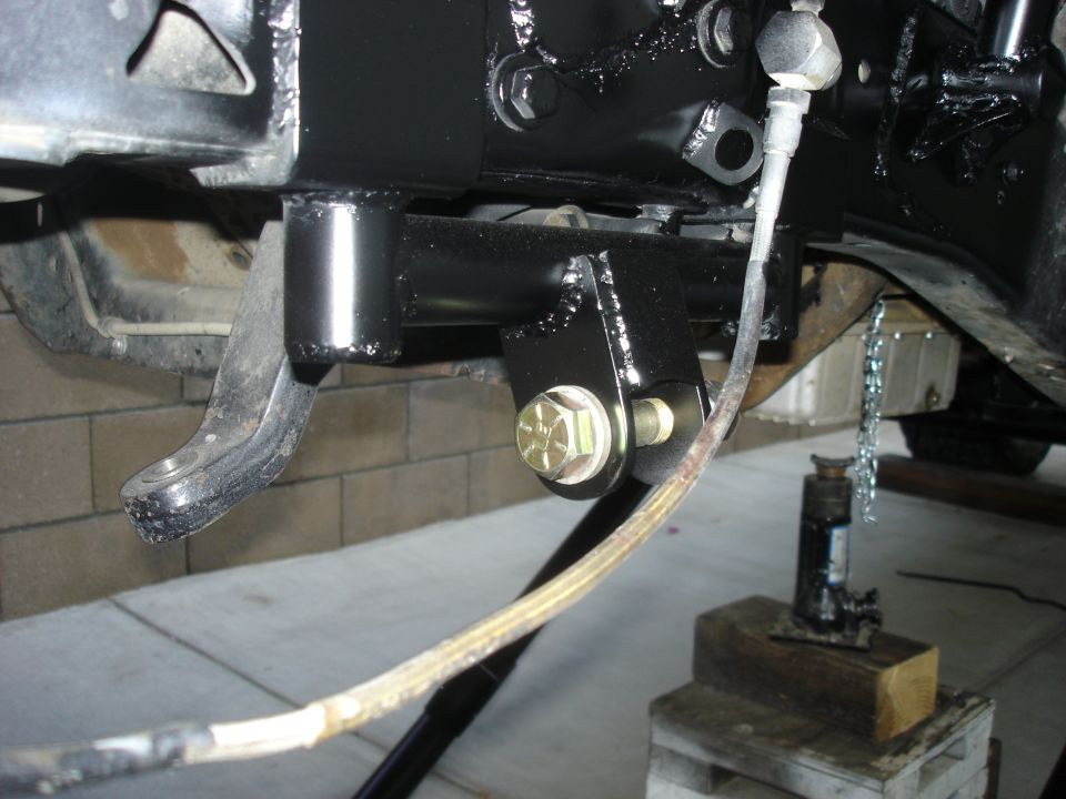 close-up of black painted vehicle frame with suspension parts and a hydraulic jack underneath