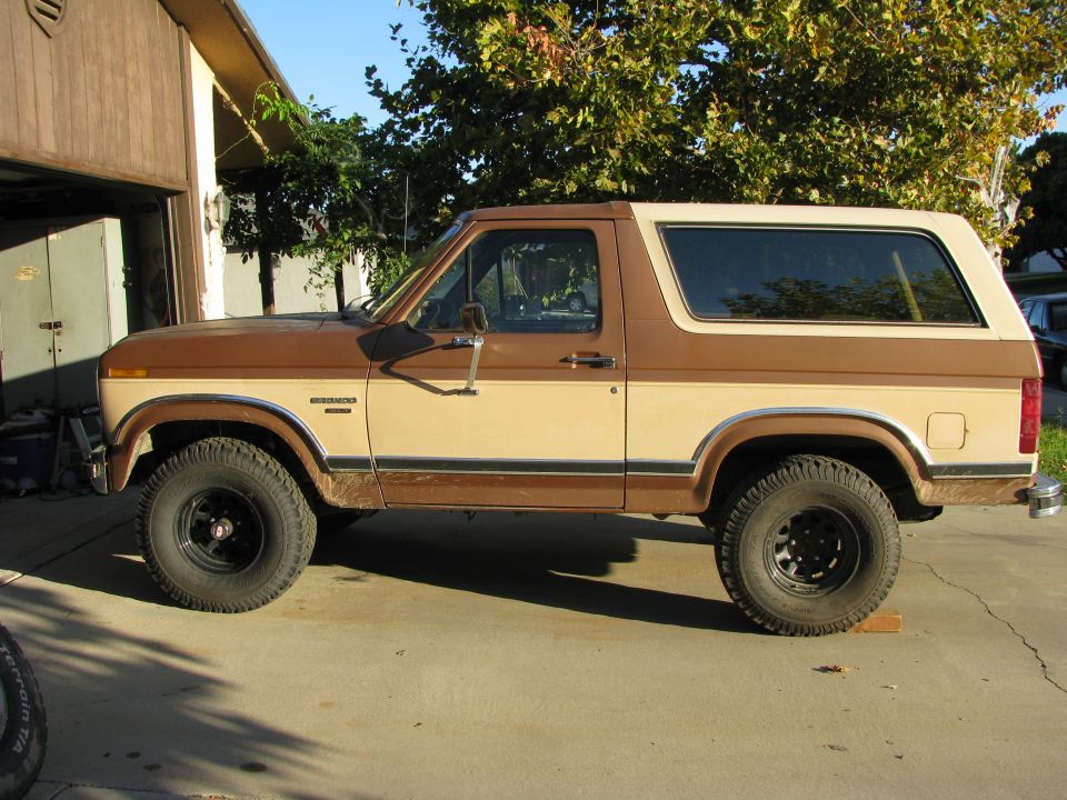 Side view of a two-tone tan and brown Ford Bronco SUV with black steel wheels on a concrete driveway