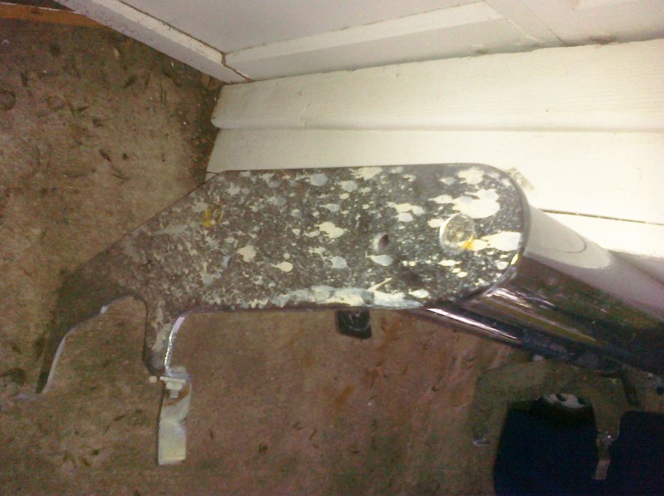 Close-up of a rusty metal bracket with some white paint splatters, attached to a chrome pipe