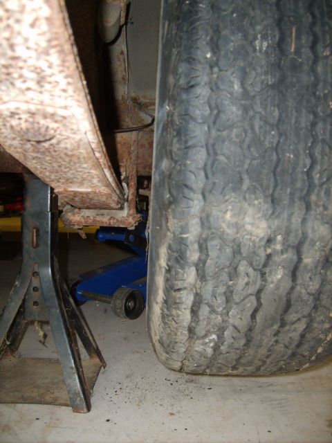 1963 Ford Galaxie - A vehicle's rear leaf spring and tire are visible, supported by jack stands and a blue hydraulic jack.