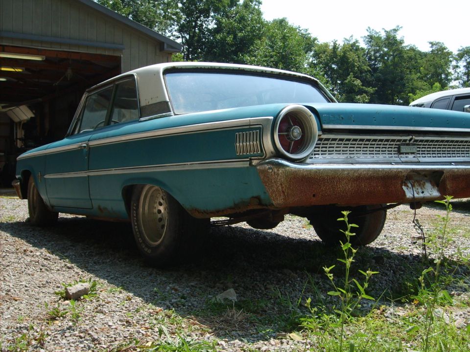 Faded teal early-1960s Ford full-size two-door hardtop parked on gravel by a shed