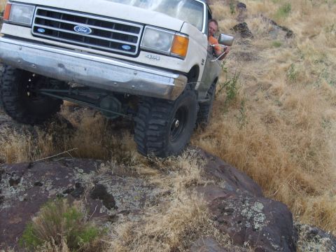 1989 Ford Bronco - A white Ford truck navigates a rocky, off-road terrain with a driver visible.