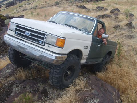 1989 Ford Bronco - A two-tone Ford F-Series truck is shown off-roading over rocks and dry grass.