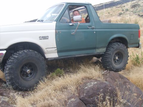 1989 Ford Bronco - A man drives a modified Ford F-250 off-road, its two-tone paint job and large tires evident.