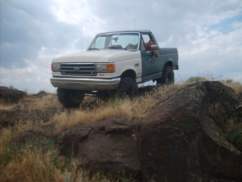 1989 Ford Bronco - A lifted Ford F-Series truck navigates a rocky, off-road landscape under a cloudy sky.