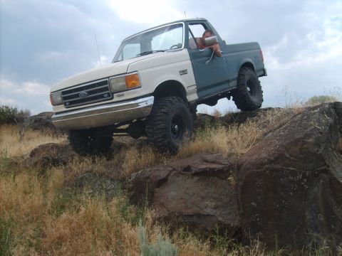 1989 Ford Bronco - A modified Ford Bronco navigates rocky terrain under a cloudy sky.