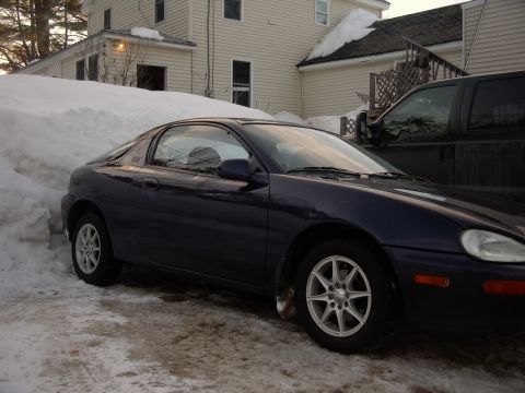 1990 Ford Bronco - A dark blue Mazda MX-3 coupe is parked in the snow beside a black pickup truck.