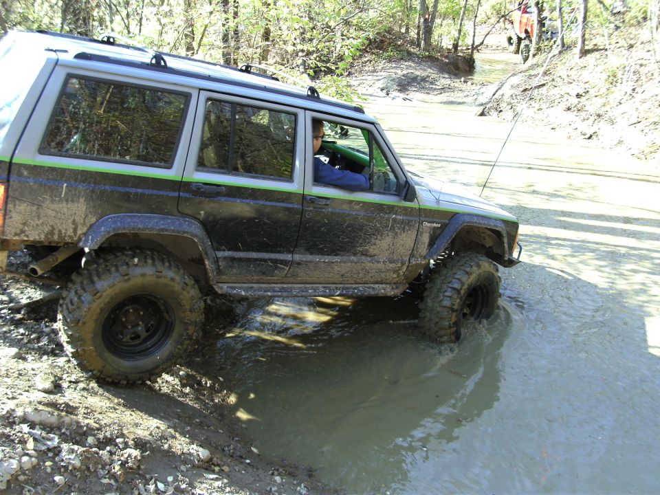 Muddy black Jeep Cherokee XJ with green stripe, side view, driving through water