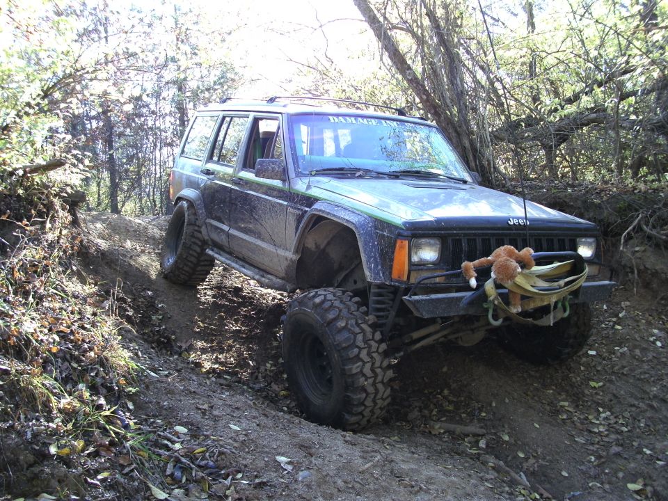Jeep Cherokee with large tires on a dirt trail, front bumper has a stuffed animal attached