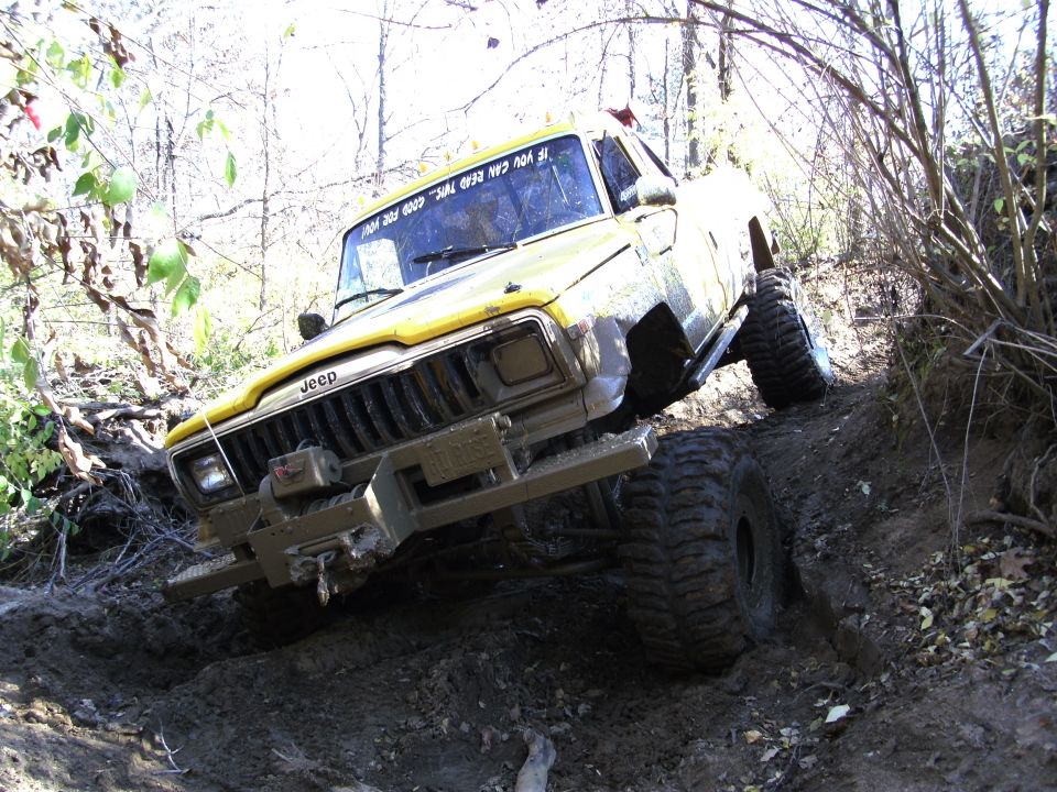 Yellow Jeep climbing a muddy hill with large tires
