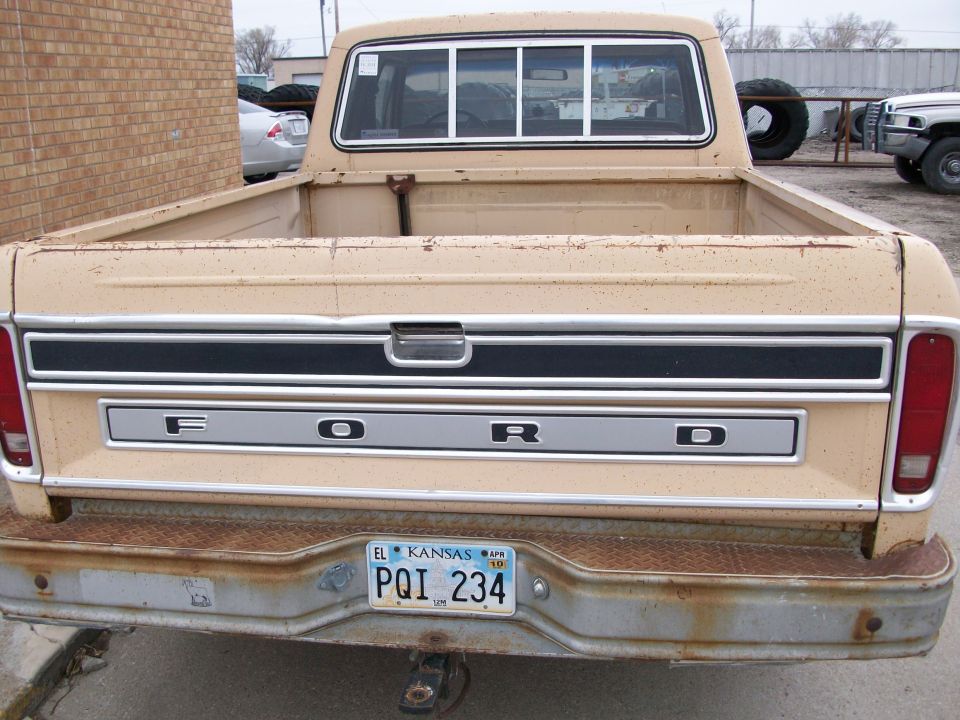 Tan 1977 Ford F-150 pickup truck rear view, showing tailgate with FORD lettering and rusty bumper
