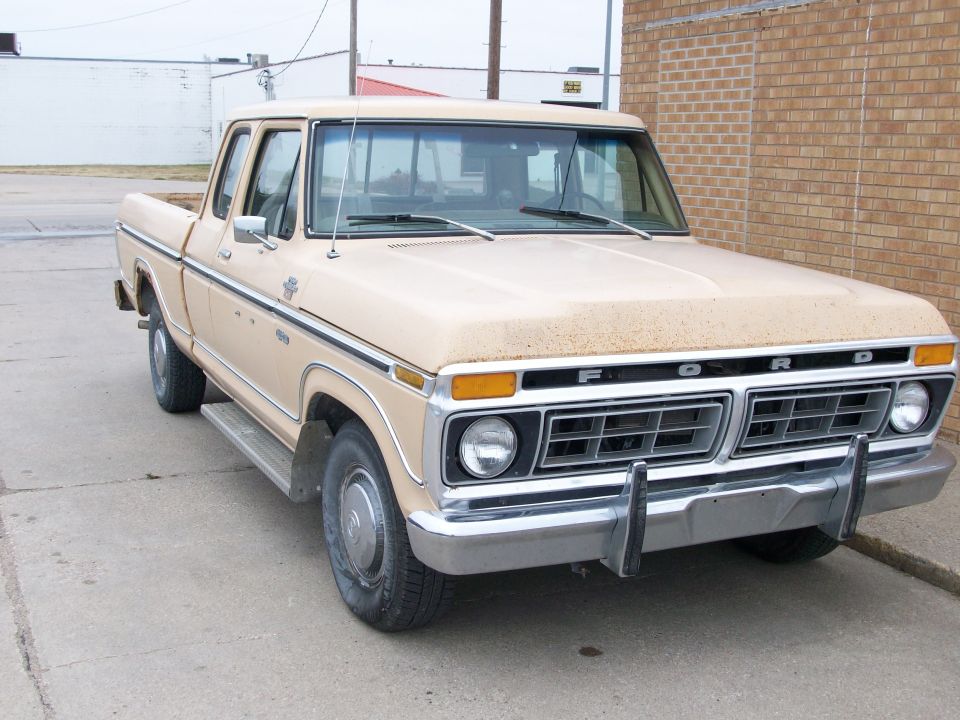 Tan Ford SuperCab pickup with chrome bumper and dog-dish hubcaps parked by a brick building