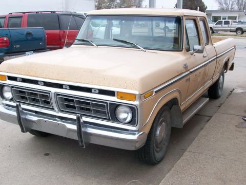 1977 Ford F-150 - A tan 1977 Ford F-150 pickup truck is parked on a paved surface with other vehicles in the background.
