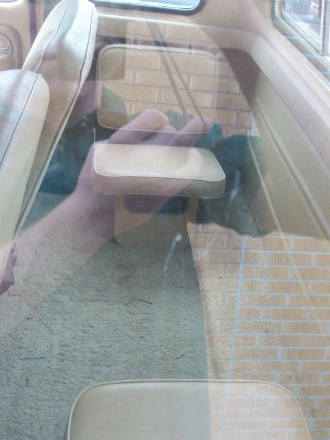 1977 Ford F-150 - Interior view of a vehicle with beige seats and carpet, showing reflections on the window.