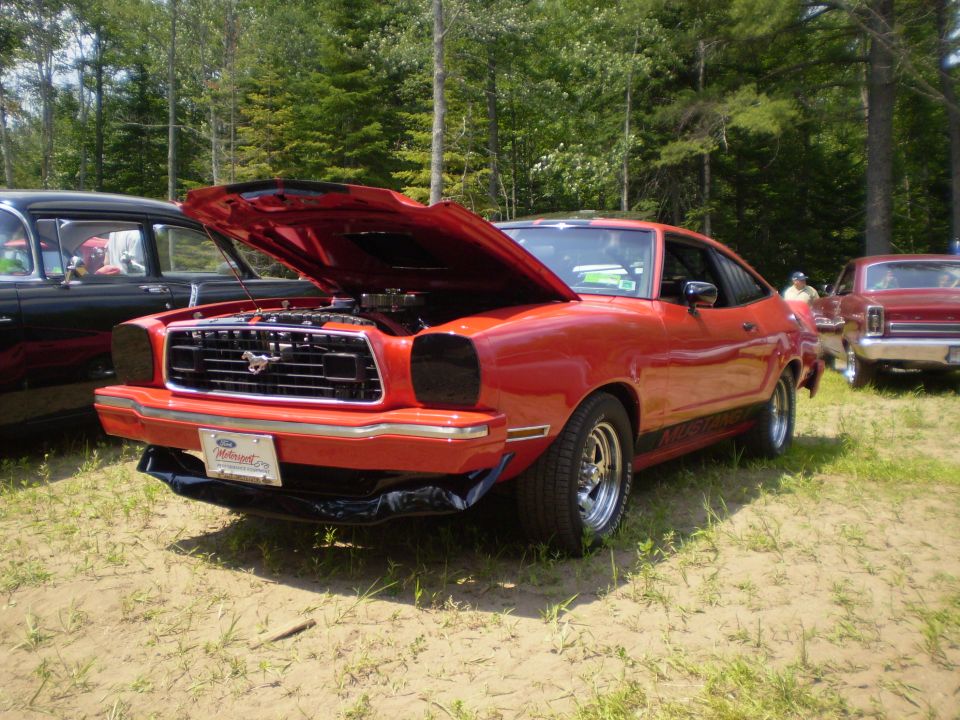 Red 1977 Ford Mustang II, hood open, parked outdoors with other cars