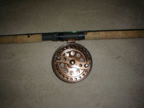 1990 Ford Bronco - A close-up view of a copper fishing reel with a perforated spool and handle.