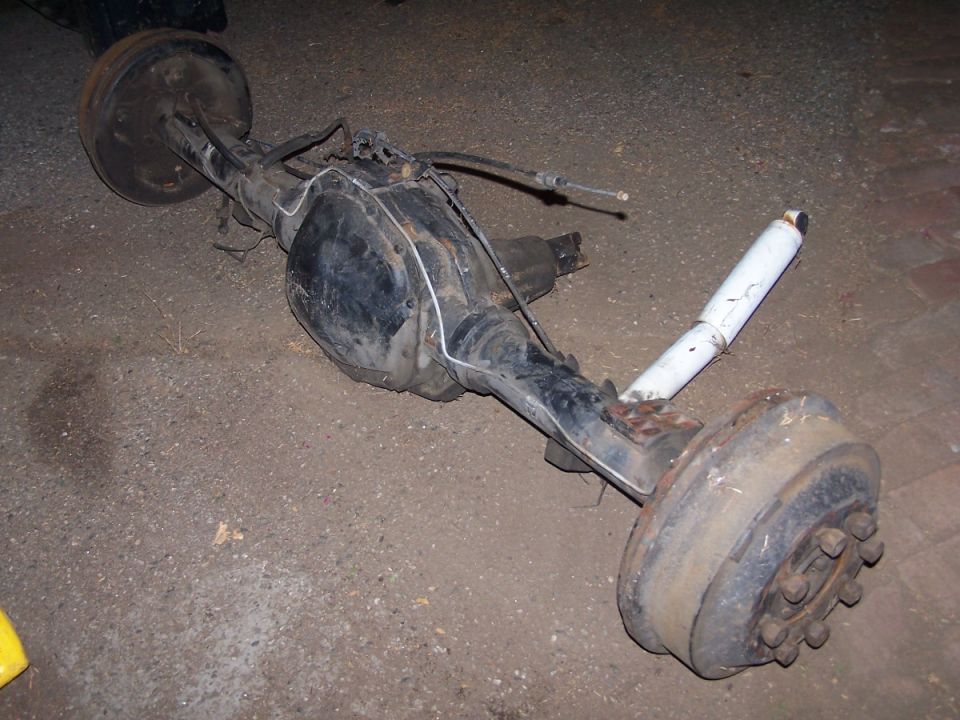 Removed rusty truck rear axle assembly lying on a paved surface at night