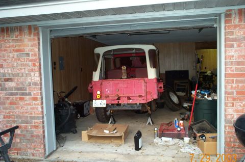 1954 Jeep Wrangler - A 1954 Jeep pickup truck, painted red and white, is parked on jack stands inside a garage, appearing to be undergoing maintenance.