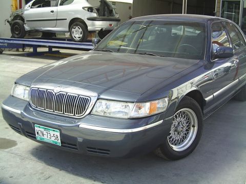 1992 Mercury Grand Marquis - A dark gray Mercury Grand Marquis is parked in front of another vehicle on a lift.