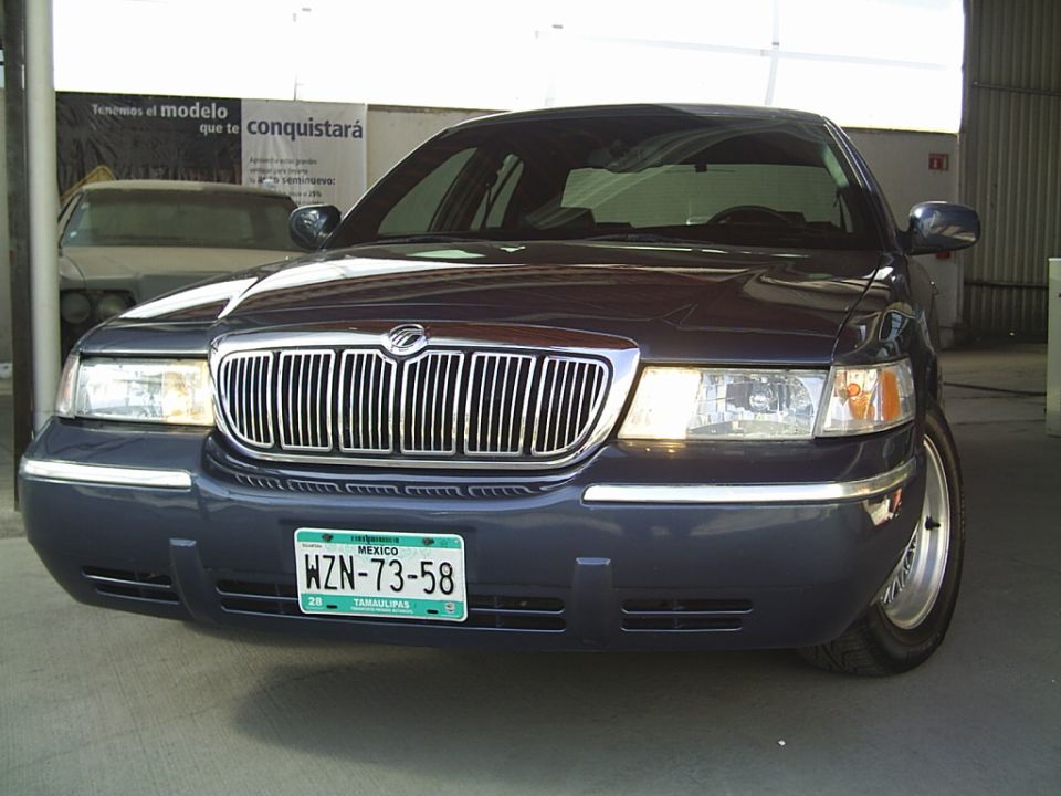 Dark blue Mercury Grand Marquis parked inside, another car behind it. Mexican license plate visible