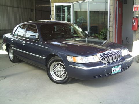 1992 Mercury Grand Marquis - A dark blue Mercury Grand Marquis is parked in front of a building with large glass windows and a red door.