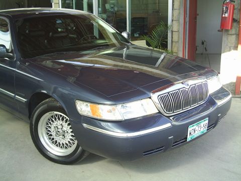 1992 Mercury Grand Marquis - A dark blue sedan with a prominent chrome grille and distinctive wire-spoke wheels is parked indoors.