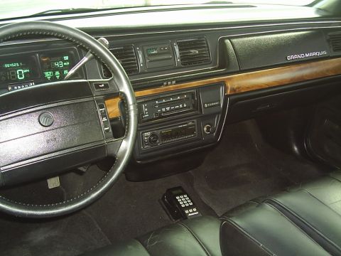 1992 Mercury Grand Marquis - The interior of a 1992 Mercury Grand Marquis features a digital dashboard, wood grain accents, and a car phone.