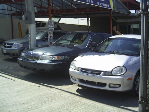 1992 Mercury Grand Marquis - Three cars are parked under a covered area. The middle car is a dark sedan, possibly a Mercury Grand Marquis.
