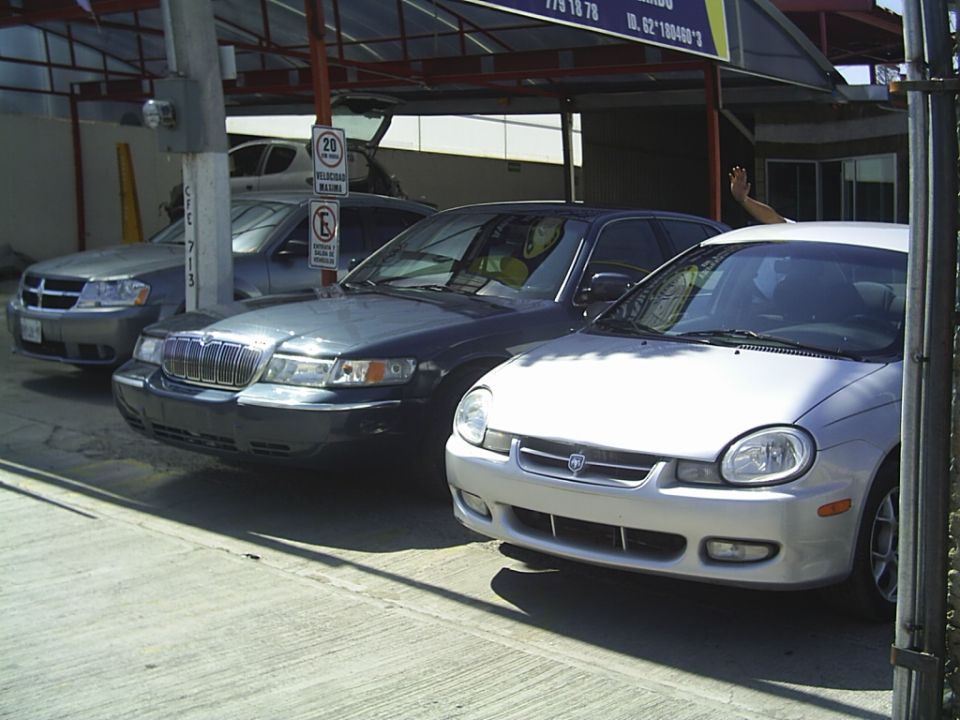 Dark sedan parked next to a silver car. A hand waves from the silver car's window