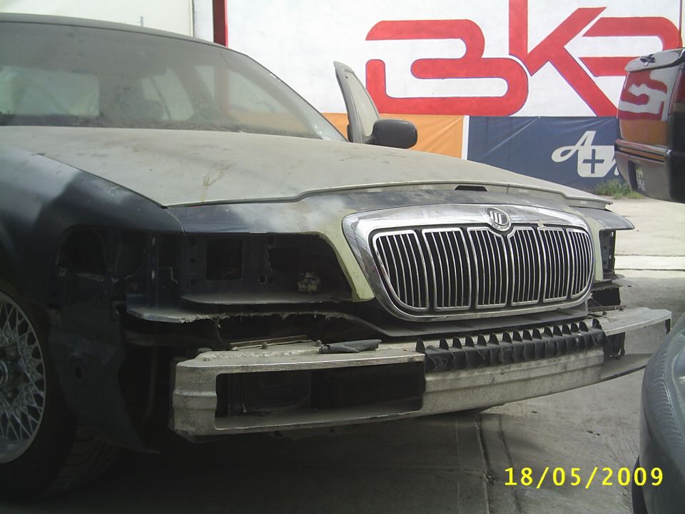 Front end of a dusty 2003 Mercury Grand Marquis with missing headlights and bumper