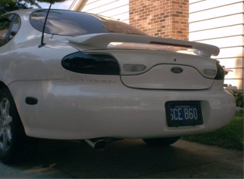 1990 Ford Taurus - The rear of a white sedan is shown, a spoiler and a license plate.