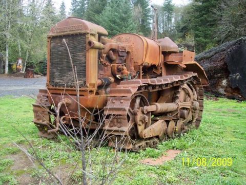 1989 Ford Bronco - This heavily rusted crawler tractor appears to be abandoned in a wooded area, with a large fallen tree nearby.
