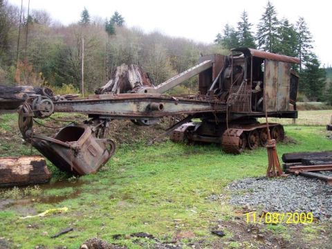 1989 Ford Bronco - An old, rusted excavator sits in a field, its large bucket resting near a log.