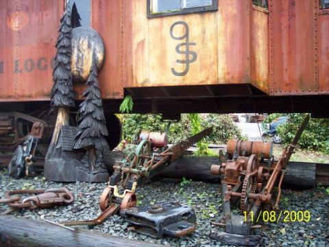 1989 Ford Bronco - A scene a weathered train car, carved wooden trees, and vintage industrial machinery displayed outdoors.