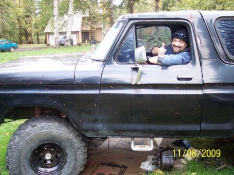 1989 Ford Bronco - A man gives a thumbs up from the driver's seat of a black Ford Bronco, with work being done underneath.