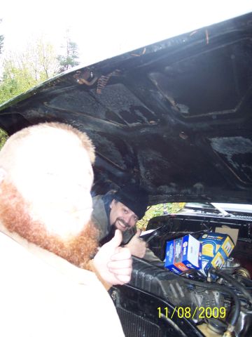 1989 Ford Bronco - Two men work on the engine bay of a vehicle, with boxes of parts visible on the engine.