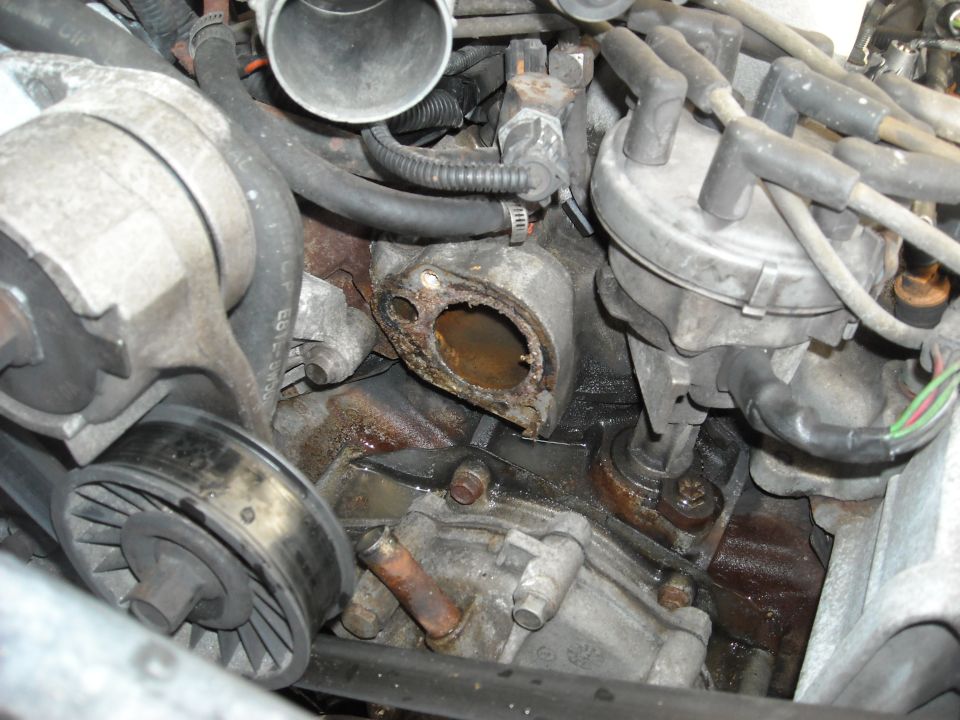 Engine bay with thermostat housing removed showing corroded coolant passage, distributor and belt pulleys visible