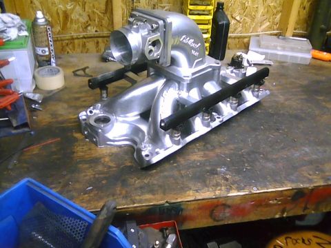 1996 Ford Bronco - Close-up of an Edelbrock intake manifold with fuel rails resting on a wooden workbench.