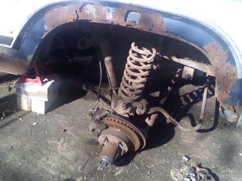 1986 Ford Bronco - Close-up of the front wheel suspension and rusted fender well of a vehicle.