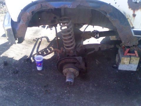 1986 Ford Bronco - Vehicle's front suspension and wheel well are heavily rusted and exposed.