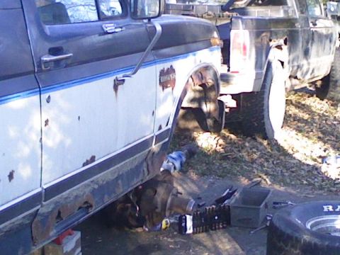 1986 Ford Bronco - A 1986 Ford Bronco is shown with its front wheel removed, revealing exposed mechanical parts and significant rust damage.