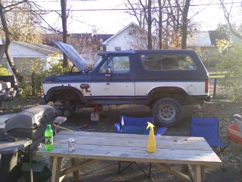 1986 Ford Bronco - This two-tone Ford Bronco appears to be undergoing maintenance, with its hood propped open and the vehicle elevated on jacks.