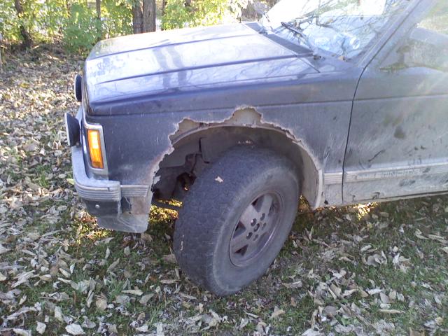 Front fender of a dark blue truck showing significant rust damage. The wheel is visible